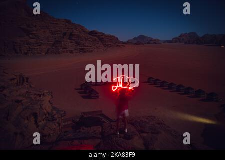 Reisender Träumer Abenteurer in wadi Rum Wüste bei Nacht Licht Malerei Wort JO als Jordanien mit Herz. Reise entdecke das Jordan Adventure Konzept Stockfoto