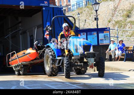 Das Küstenrettungsboot wird in Cromer, Großbritannien, aus der Garage genommen. Rettungsboot Mann zieht Boot mit Traktor zum Meer. Stockfoto