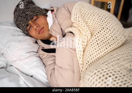 Unwohl Mann Mieter in Decke schlafen im kalten Schlafzimmer. Leiden Sie an mangelnder Hitze. Ungesunder junger Mann kämpft zu Hause mit der Kälte. Keine Heizung Stockfoto