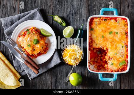 Vegetarische Enchilada-Kasserolle mit Tortillas, Sauce, Pinto-Bohnen, Mais, Zucchini und mexikanischem Käse in Backform und auf weißem Teller, Stockfoto