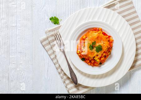 Vegetarische Enchilada-Kasserolle mit Tortillas, Sauce, Pinto-Bohnen, Mais, Zucchini und mexikanischem Käse auf weißem Teller, flacher Laie Stockfoto