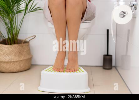 Frau, die auf der Toilette saß und ihre Füße auf einen Hocker setzte Stockfoto