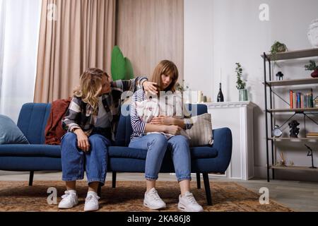 Besorgte Mutter versucht, ihre beleidigte Tochter, die im Wohnzimmer auf der Couch sitzt, zu beruhigen Stockfoto