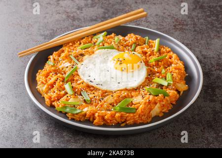 Koreanischer Kimchi gebratener Reis mit Ei, grüner Zwiebel und Sesam in Nahaufnahme auf einem Teller auf dem Tisch. Horizontal Stockfoto