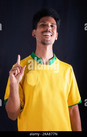 Brasilianischer Fußball Black Player Fan mit gelbem Shirt feiern, isoliert auf schwarzem Hintergrund. Stockfoto