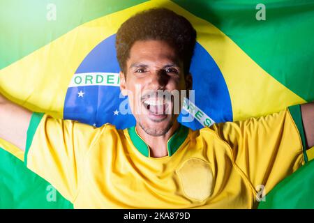 Brasilianischer Fußballfan - Schwarzer Mann Hält Die Brasilianische Flagge Hinter Der Feier Stockfoto