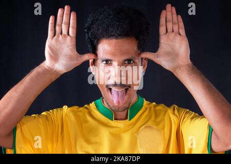 Brasilianischer Fußball Black Player Fan mit gelbem Shirt feiern, isoliert auf schwarzem Hintergrund. Stockfoto