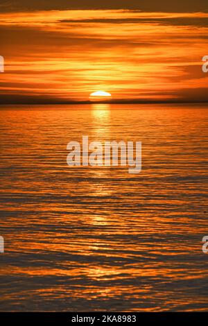 Eine vertikale Aufnahme eines faszinierenden Sonnenuntergangs, der sich im Meer spiegelt Stockfoto