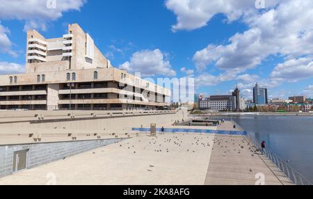 Kazan, Russland - 6. Mai 2022: Außenansicht des Akademischen Theaters Galiaskar Kamal Tatar. Blick auf die Straße, normale Menschen gehen an einem sonnigen Tag an der Küste des Lake Kaban spazieren Stockfoto