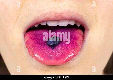 Eine Person zeigt eine Indikatorpille auf seiner Zunge, um Plaque zu bestimmen. Stockfoto