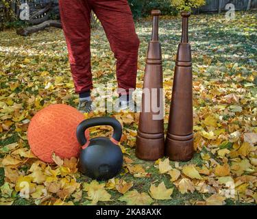 Schwere eiserne Kugelhantel, Slam Ball und hölzerne persische Clubs in einem Hinterhof, Herbstlandschaft Stockfoto