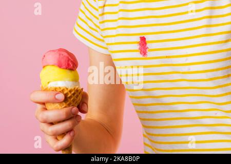 Cremiges Erdbeereis auf die Kleidung geben. Die Hand eines Mädchens hält einen Eiskegel mit drei Messern. Stockfoto