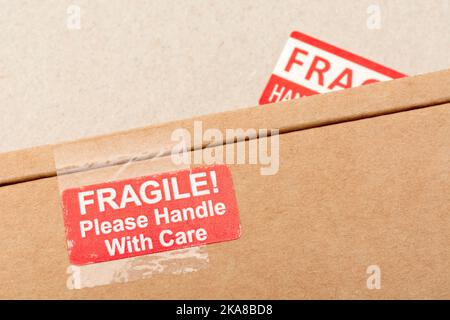 Versandkartons aus braunem Karton mit rot-weißem Aufkleber auf Haftpapier, bedruckt mit „Fragile“ und „Handle with Care“. Für etwas zerbrechliches und delikates Stockfoto