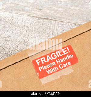 Versandkartons aus braunem Karton mit rot-weißem Aufkleber auf Haftpapier, bedruckt mit „Fragile“ und „Handle with Care“. Für etwas zerbrechliches und delikates Stockfoto