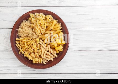 Verschiedene Arten und Formen der italienischen Pasta in Keramik-Platte auf weißem Holzhintergrund mit Kopie Spase Stockfoto