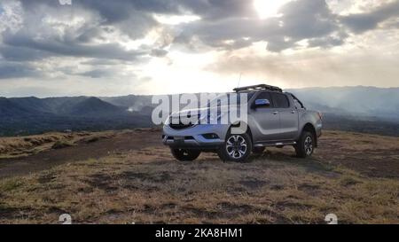 Grauer Pick-up-Truck auf dem Hintergrund des Vulkans in der Sonnenuntergangszeit Stockfoto