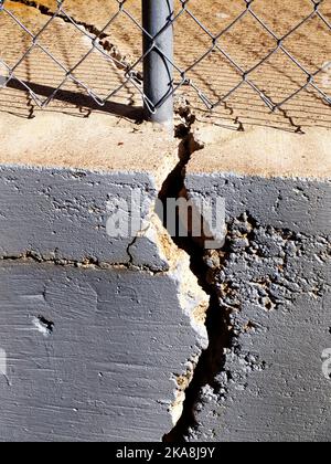 Kettengliederzaun und Mast auf rissiger Zementwandstruktur Stockfoto