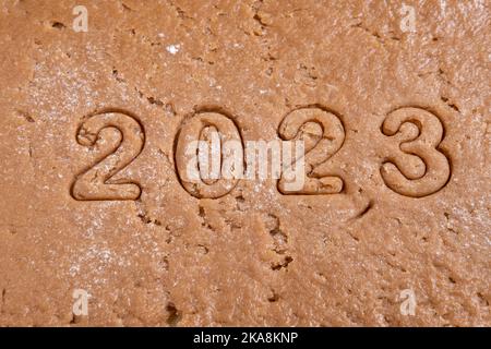 Die Zahlen des Jahres 2023 werden aus Lebkuchenteig für Weihnachtskekse ausgeschnitten. Kochen hausgemachter Lebkuchen. Schneiden Sie das Neujahrsdatum ab Th Stockfoto