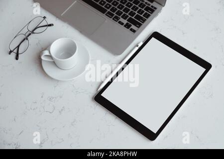 Geöffneter Laptop mit digitalem Tablet mit weißem leerem Bildschirm. Auf Marmortisch, Arbeitsplatz Stockfoto