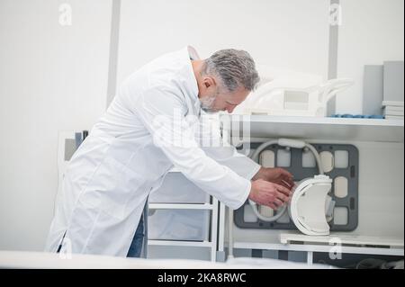 Grauhaariger Arzt in einem Laborkittel, der einen MRT-Scanner vorbereitet Stockfoto