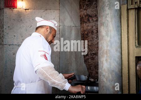 Bild eines Mannes, eines Küchenchefs, eines Kebab-Meisters, der sich vorbereitet, etwas Fleisch eines Kebab-Spießes zu schneiden, um ein Döner-Kebab-Sandwich zuzubereiten. Döner Kebab hat auch dön geschrieben Stockfoto