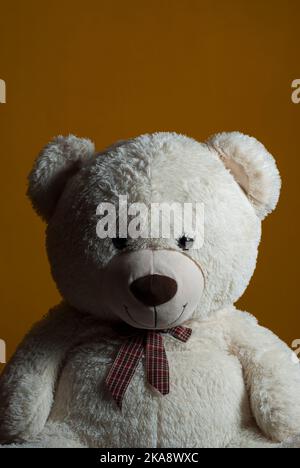 Weißer Teddybär mit Schleife auf vertikaler Seite mit dunklem Hintergrund mit Bereich für Kopierraum Stockfoto