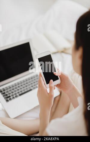 Rückansicht der jungen Frau mit Smartphone und Laptop mit leerem Bildschirm. Stockfoto