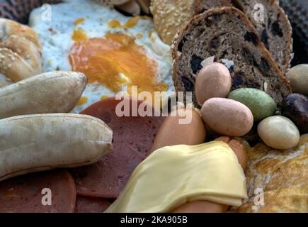Hausgemachtes Frühstück mit gebratenen Würstchen, Bologna Würstchen, Käse, Obstbrot, gebratene Kuchen, Spiegelei, Omelett, Banane, Schokoladenkekse und Knoblauch Stockfoto