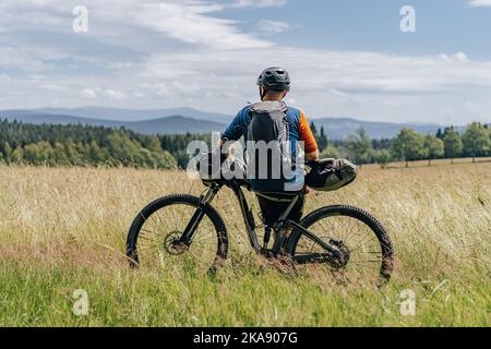 Bikepacking in den Bergen. Mann, der mit seinem Fahrrad und Rucksack auf einer Wiese steht, bereit für eine Bikepacking-Abenteuerfahrt. Stockfoto