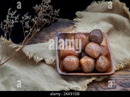 Drei aromatisierte, konservierte chinesische Pflaumen (konservierte Früchte) auf Holzplatte. Sein Geschmack ist sauer, salzig und süß. Leerzeichen für Text, selektiver Focu Stockfoto