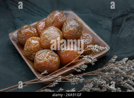 Drei aromatisierte, konservierte chinesische Pflaumen (konservierte Früchte) auf Holzplatte. Sein Geschmack ist sauer, salzig und süß. Leerzeichen für Text, selektiver Focu Stockfoto