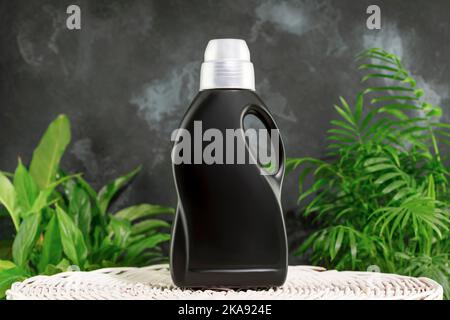 Natürliches Waschmittel-Mockup zum Waschen schwarzer Kleidung. Waschmittelkonzept mit einer Flasche Waschgel oder Weichspüler auf dem Wäschekorb Stockfoto