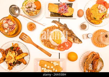 Overhead-Bild von peruanischen und ecuadorianischen Gerichten mit süßen Kochbananen, Ceviches, Fischsuppe, gegrilltem Fisch und Chaufa-Reis mit Bohnen und Chili Stockfoto