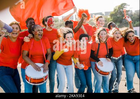 Eine Gruppe von Sportfans mit roten T-Shirts und bemalten Gesichtern jubelt ihr Team an Stockfoto