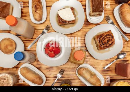 Typische venezolanische und lateinische Desserts, Golfeados, Cremes, Quesillos, gefüllte Stücke und Erdbeertartlet auf einem verkohlten Kiefernholztisch Stockfoto