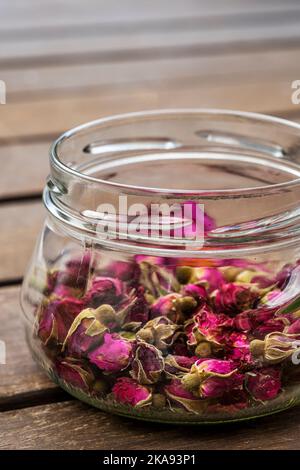 Schöne Glasgläser mit Teerosen auf Akazienplankenoberfläche Stockfoto