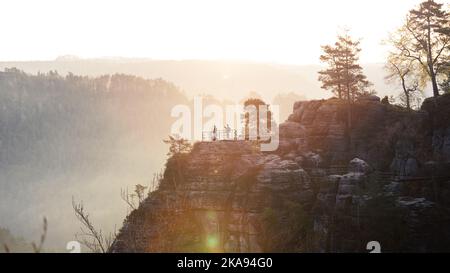 Eine Silhouettenaufnahme von zwei Touristen und Bäumen auf den Bastei-Felsen im Nationalpark Sächsische Schweiz bei Sonnenuntergang. Dresden, Deutschland Stockfoto