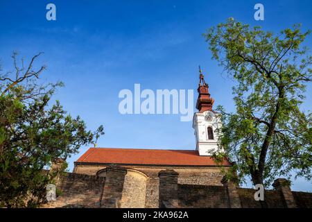 Bild des ikonischen Uhrturms der serbischen orthodoxen Kirche von Stari Slankamen, in Serbien, aufgenommen während eines warmen Sonnenuntergangs. Stari Slankamen auch bekannt Stockfoto