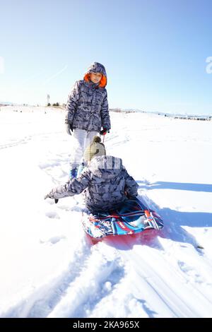 Kinder lachen haben Spaß Rodeln an einem sonnigen Tag im Winter denver Stockfoto