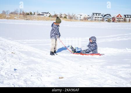 Kinder lachen haben Spaß Rodeln an einem sonnigen Tag im Winter denver Stockfoto