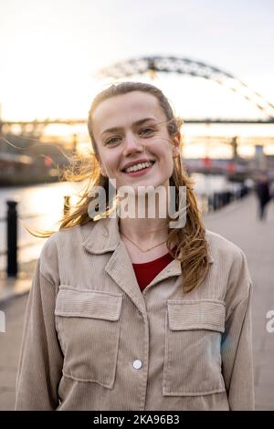 Ein Porträt einer jungen Frau, die den Tag in Newcastle upon Tyne verbringt. Sie schaut auf die Kamera und schmillt, während die Sonne hinter ihr scheint. Stockfoto