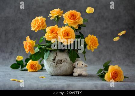 Strauß cremefarbener Rosen in einem Blumentopf, schwebende Blütenblätter und Spielzeug-Schafe auf grauem Hintergrund Stockfoto
