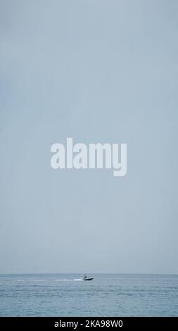 Ein kleines Boot, das auf einem ruhigen Meer vor einem nebligen Hintergrund fährt Stockfoto