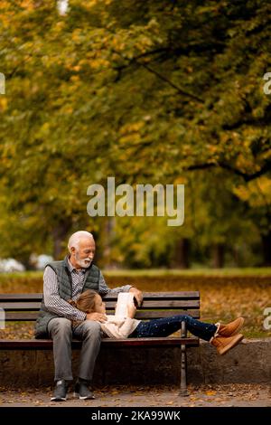 Der gutaussehende Großvater verbringt am Herbsttag Zeit mit seiner Enkelin auf der Bank im Park Stockfoto