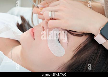 Nahaufnahme der kaukasischen Frau Client liegend mit geschlossenen Augen während Wimpern Verlängerung Verfahren. Details der falschen Wimpern machen Prozess Stockfoto