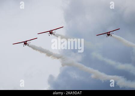 Drei kleine rote Sportflugzeuge mit Rauchstreifen machen während einer Flugshow einen Parallelflug Stockfoto