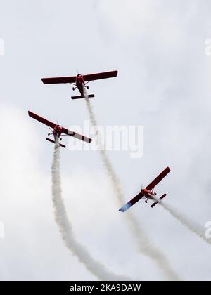 Drei rote Sportflugzeuge mit Rauchpfaden fliegen während einer Flugshow in Kunstflugform Stockfoto