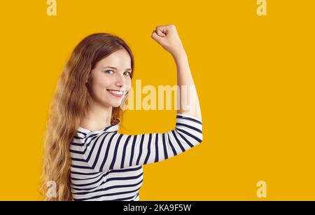 Glückliche, selbstbewusste, starke junge Frau, die ihre Kraft zeigt, ihren Arm beugt und lächelt Stockfoto
