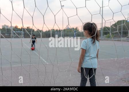 Rückansicht des Kindertorhüters bereit, einen Fußballstand auf dem Fußballplatz im Fußballtor zu fangen. Selektiver Fokus auf Mädchen. Stockfoto