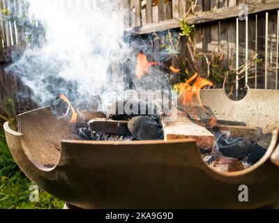 Brennendes Holz und Kohle in einer Metallfeuerschüssel mit viel Rauch Stockfoto